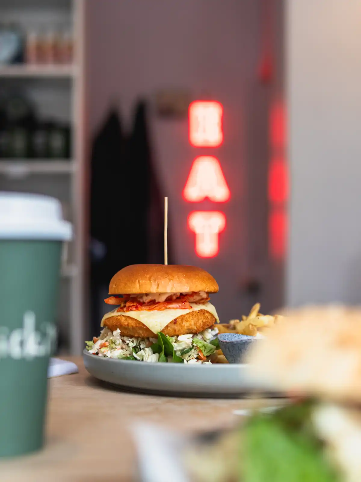 Professional food photography of a vegan burger with restaurant interior and neon sign in background